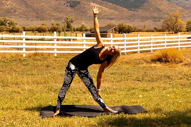 Yoga teacher demonstrating pose in Utah field near mountains.